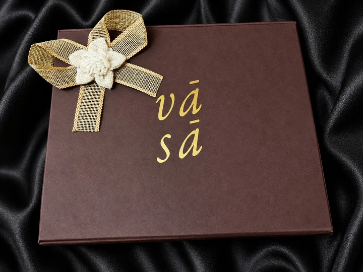 A dark VASA gift box with a gold ribbon and a woven flower, on black satin